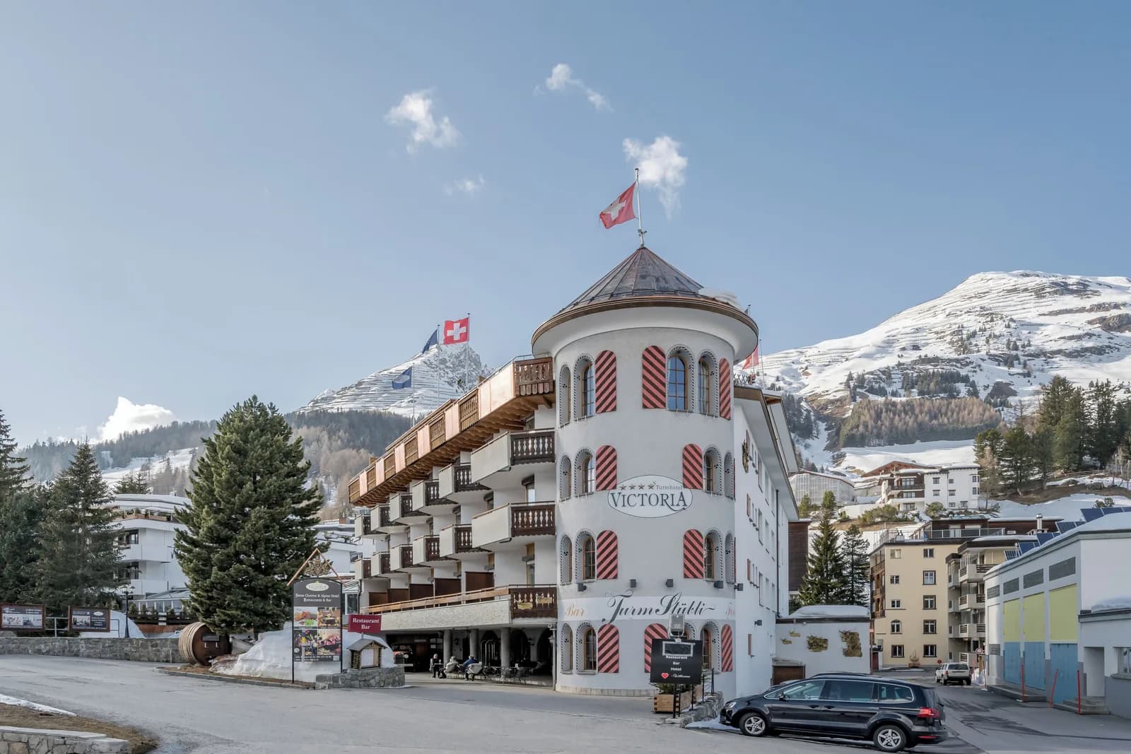 The Turmhotel Victoria in Davos, a classic Swiss alpine hotel with a distinctive round tower, below the snow-covered mountains.