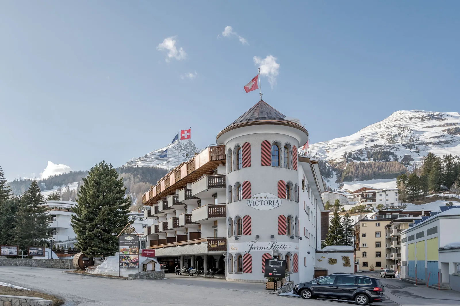 The Turmhotel Victoria in Davos, a classic Swiss alpine hotel with a distinctive round tower, below the snow-covered mountains.